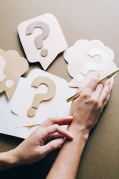 Photo of paper question marks with hands and a pen suggesting curiosity and inquiry.